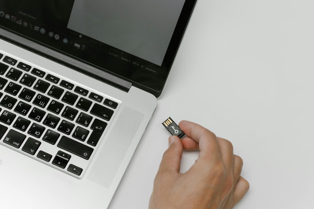 A person holds a USB flash drive near the port of an open laptop with a Russian keyboard. The scene suggests data transfer or connectivity.
