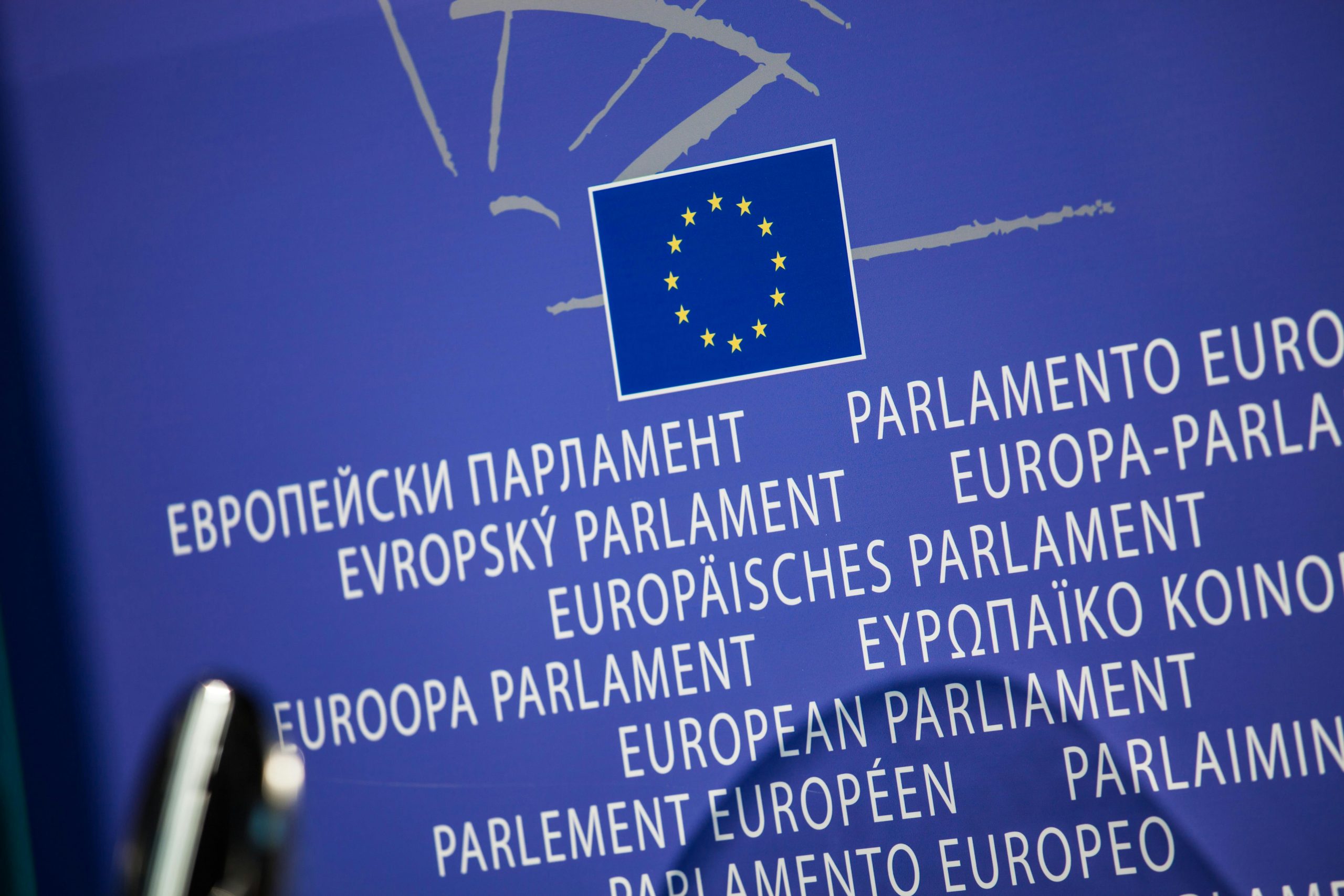 Blue backdrop featuring the European Union flag above "European Parliament" in multiple languages, conveying international unity and governance.