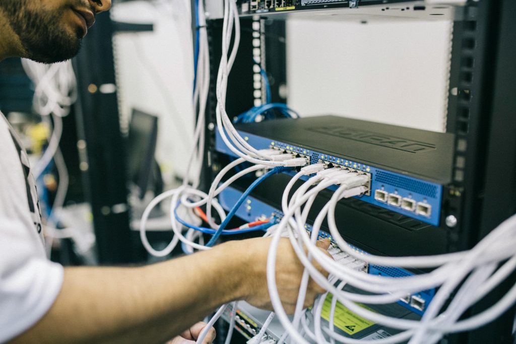 A person connects multiple white cables to a network switch in a server rack. The scene conveys a sense of focus and technical work.